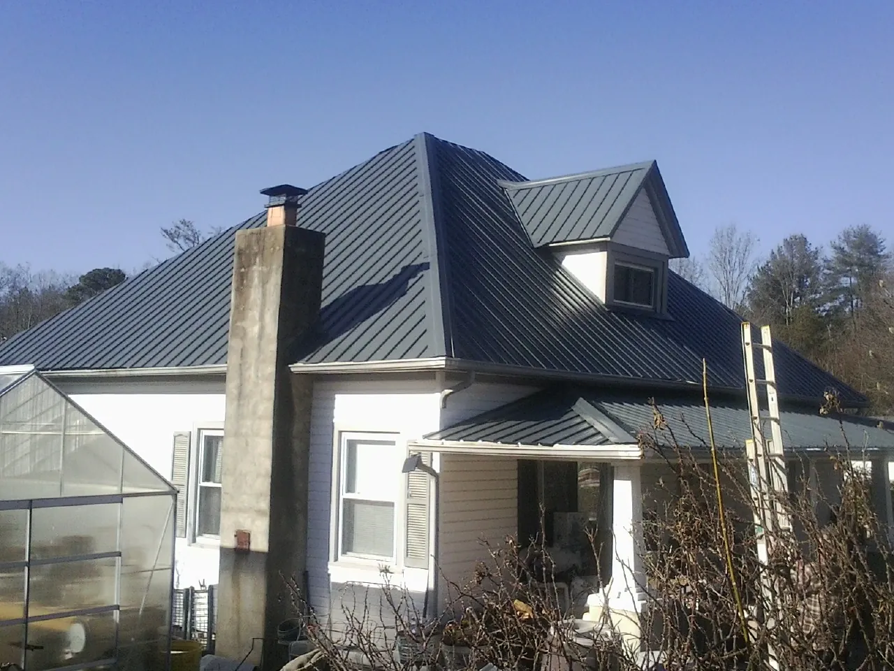 Dark blue standing seam metal roof on a white farmhouse with dormer — Slate & Tile Roof Repair by Roofing Brothers in Star City