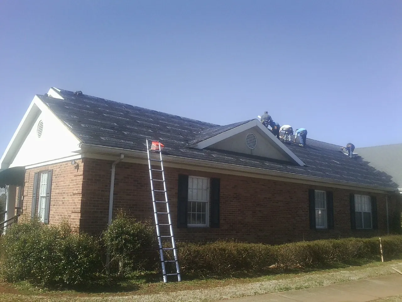 Crew tearing shingles off a brick ranch roof with a ladder set — Metal Roof Repair work by our crew in Star City