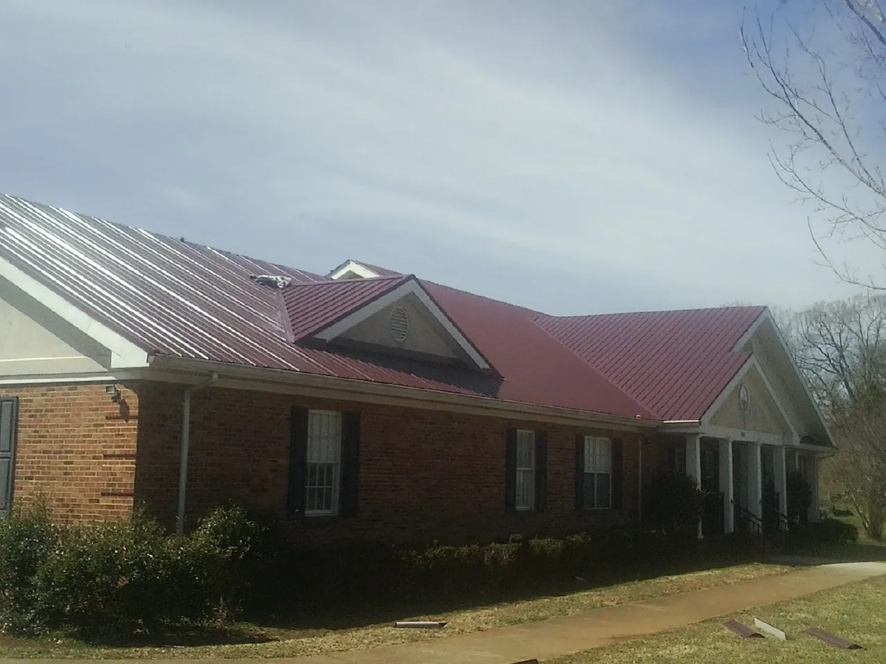 Red metal roof with gabled entries on a long brick building, from a Hail Damage Roof Repair job in Star City