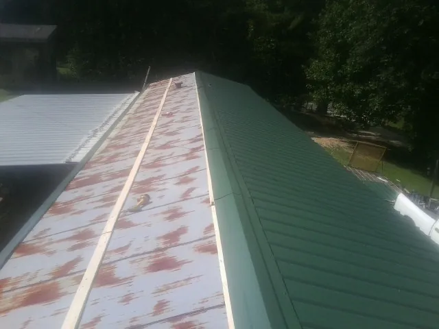 Old rusted panels beside newly installed green metal roofing — Wind Damage Roof Repair by Roofing Brothers in Star City