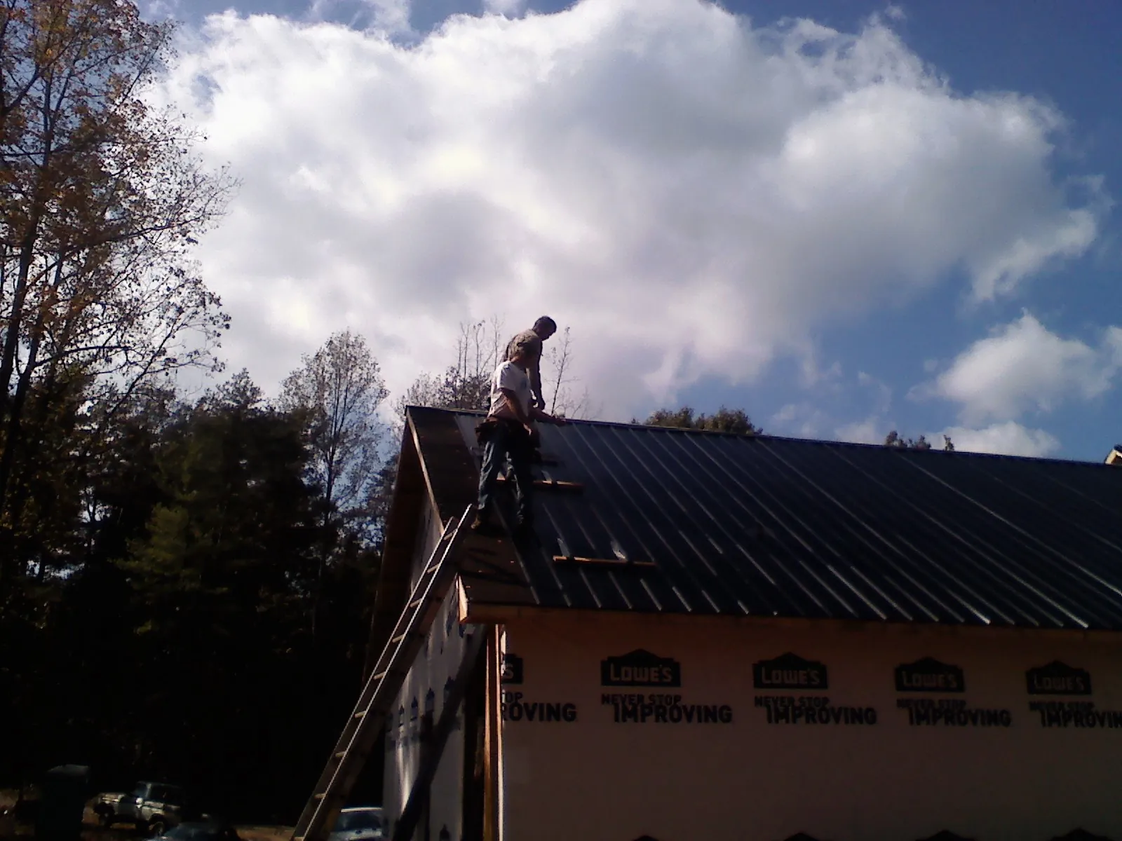 Roofer fastening dark metal panels high against a cloudy sky, from a Roof Inspection job in Star City