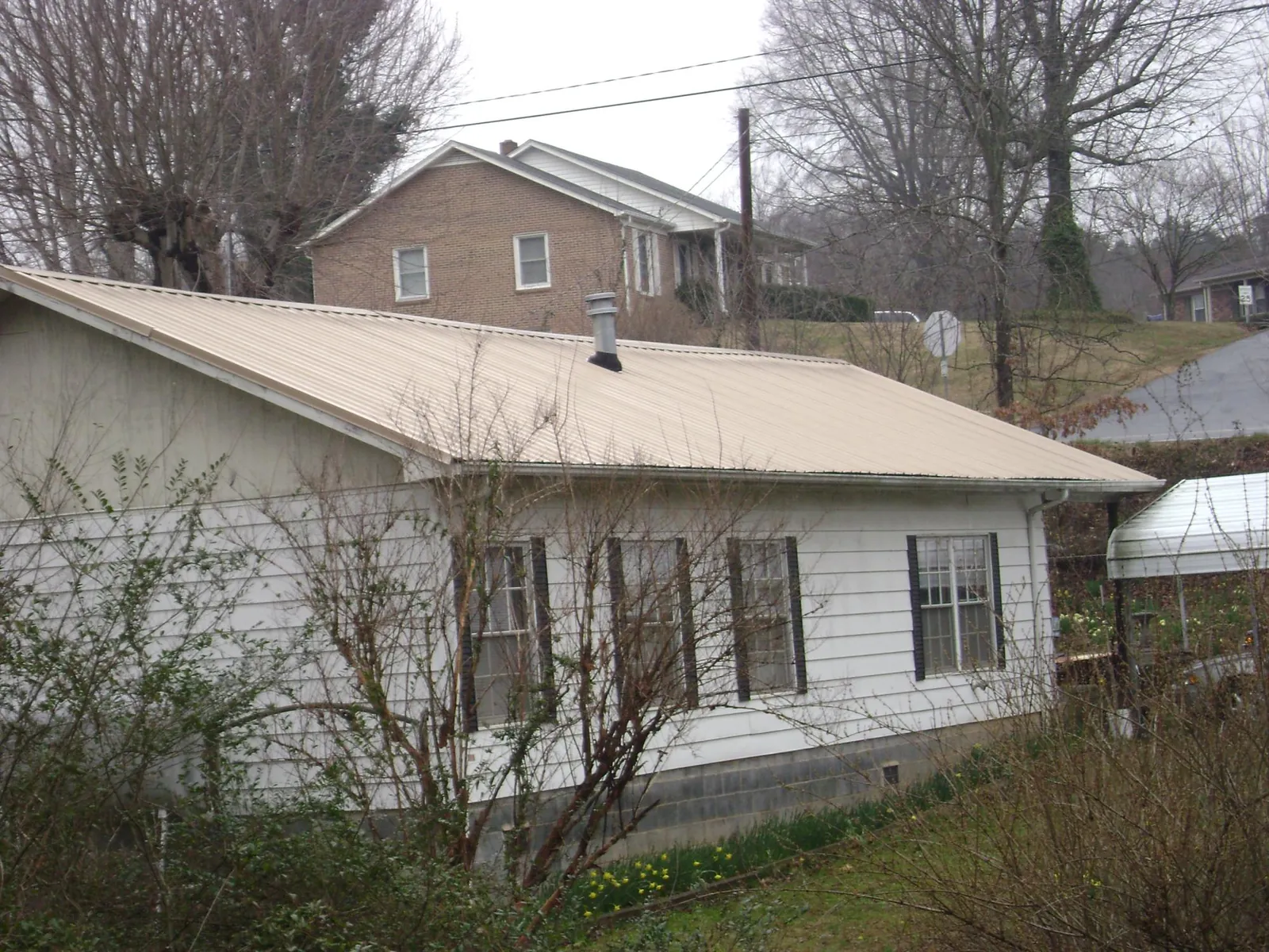 Tan metal roof on a white sided house set into a hillside — Commercial Roofing by Roofing Brothers in Star City
